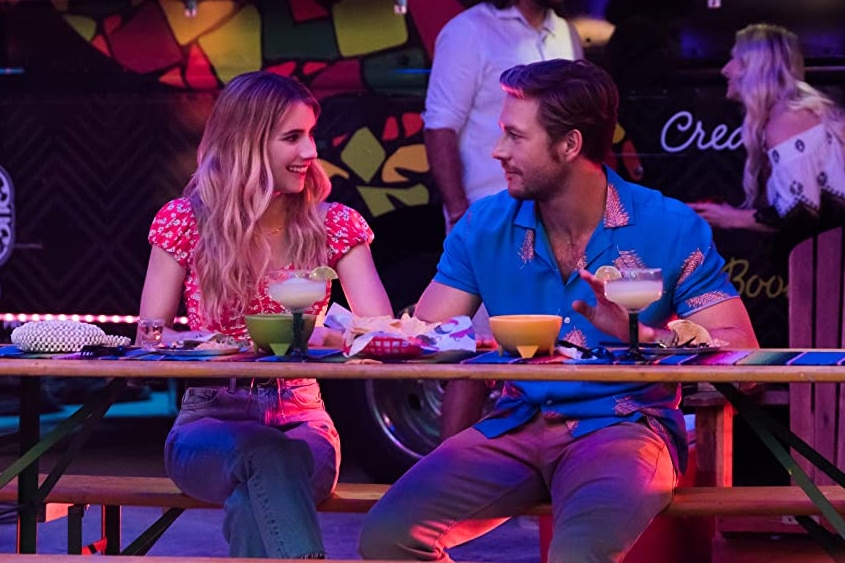 Emma Roberts and Luke Bracey in a scene from Holidate, sitting at a table with margaritas and nachos