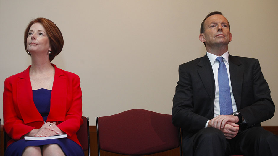 Tony Abbott and Julia Gillard sit next to each other separated by a seat