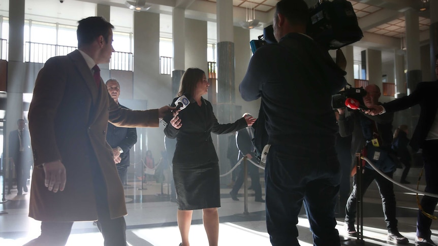 Jacquie Lambie raises her hands while walking as journalists scurry around her in Parliament House.