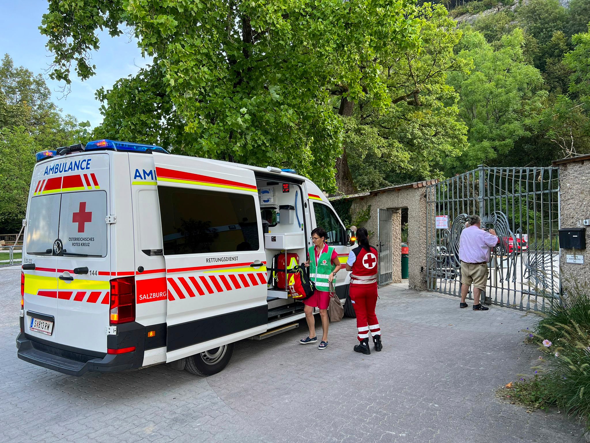 An ambulance standing outside zoo gates with two medics standing outside it