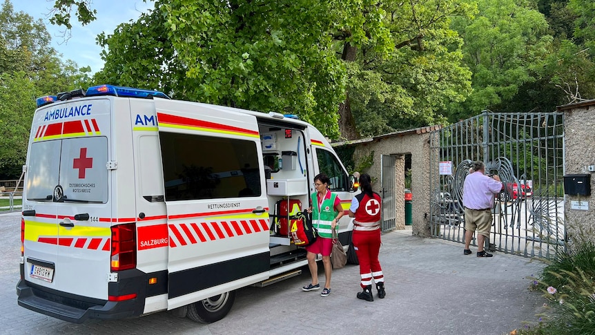 An ambulance standing outside zoo gates with two medics standing outside it