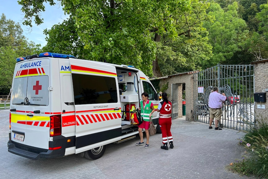 An ambulance standing outside zoo gates with two medics standing outside it
