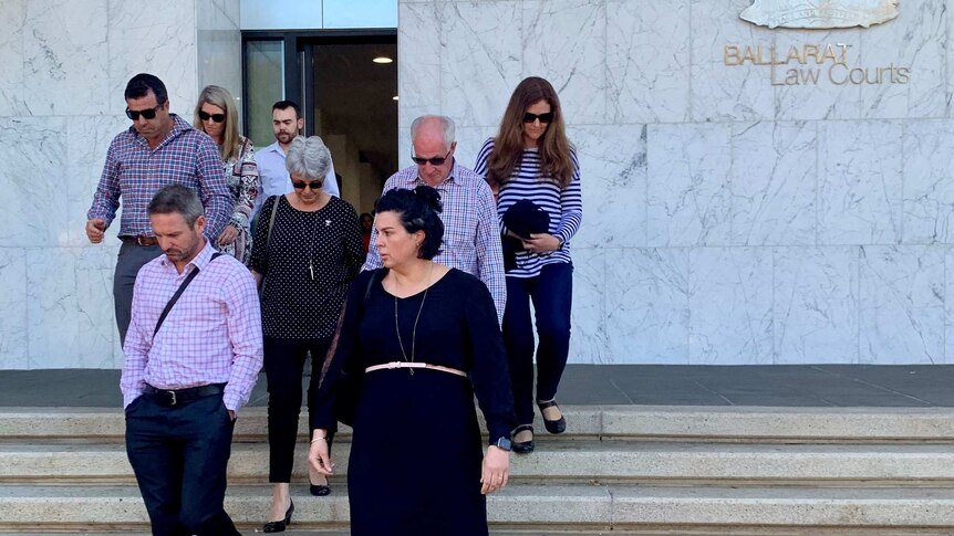 A woman in her sixties, her family, and lawyer, walk down the stairs in front of the Ballarat Courthouse