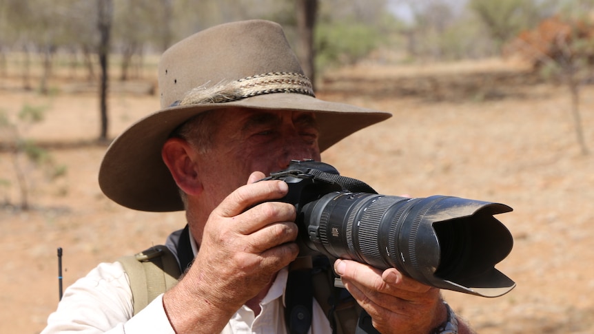 Alan Davey squints through the viewfinder of an SLR camera with a telephoto lens.