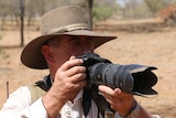 Alan Davey squints through the viewfinder of an SLR camera with a telephoto lens.