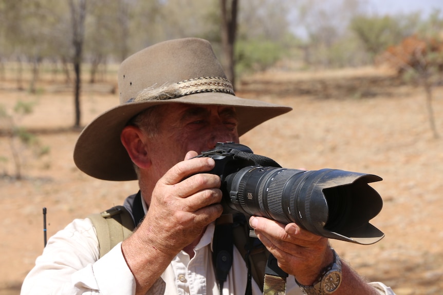 Alan Davey squints through the viewfinder of an SLR camera with a telephoto lens.