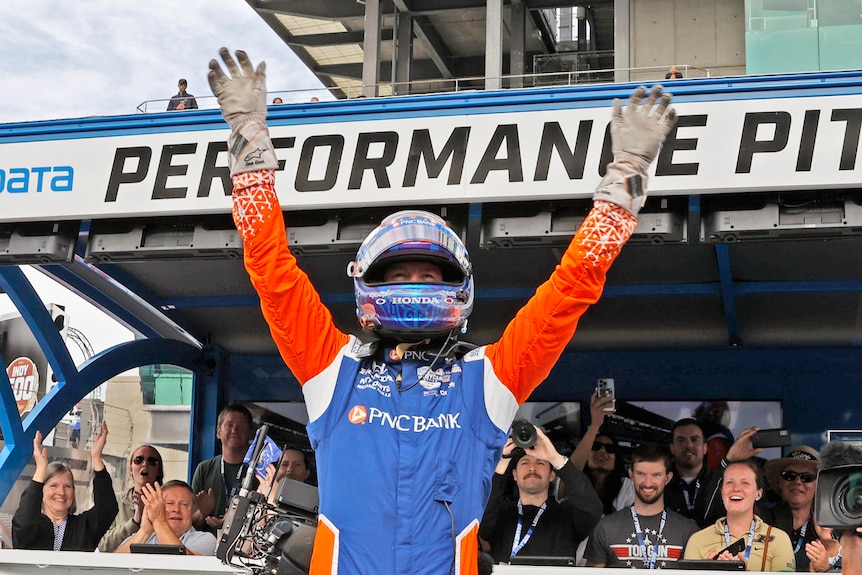 Scott Dixon raises his hands while wearing his helmet