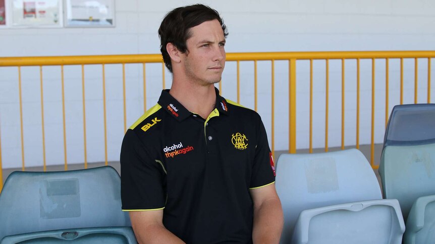 A mid shot of Hilton Cartwright sitting in the stands at the WACA Ground wearing a black and yellow WA shirt.
