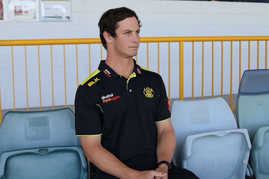 A mid shot of Hilton Cartwright sitting in the stands at the WACA Ground wearing a black and yellow WA shirt.