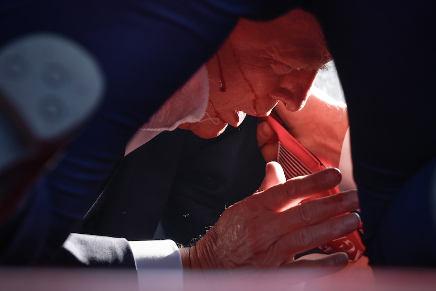 Trump is seen in profile close up with a bloodied face and hands on the ground