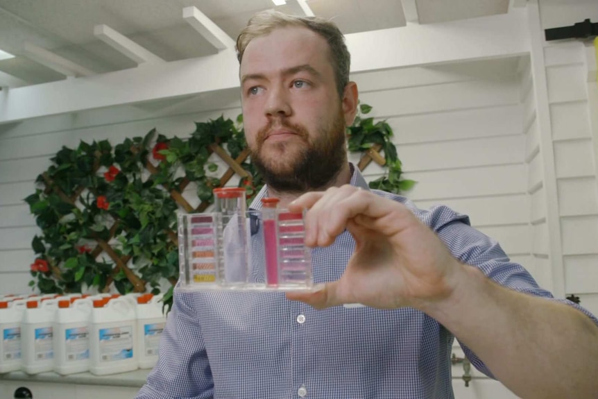 Jarrod Cullen holds up a solution testing kit with pink liquid in it.