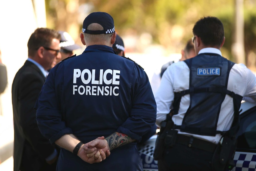 Police officers stand outside a house next to police cars.