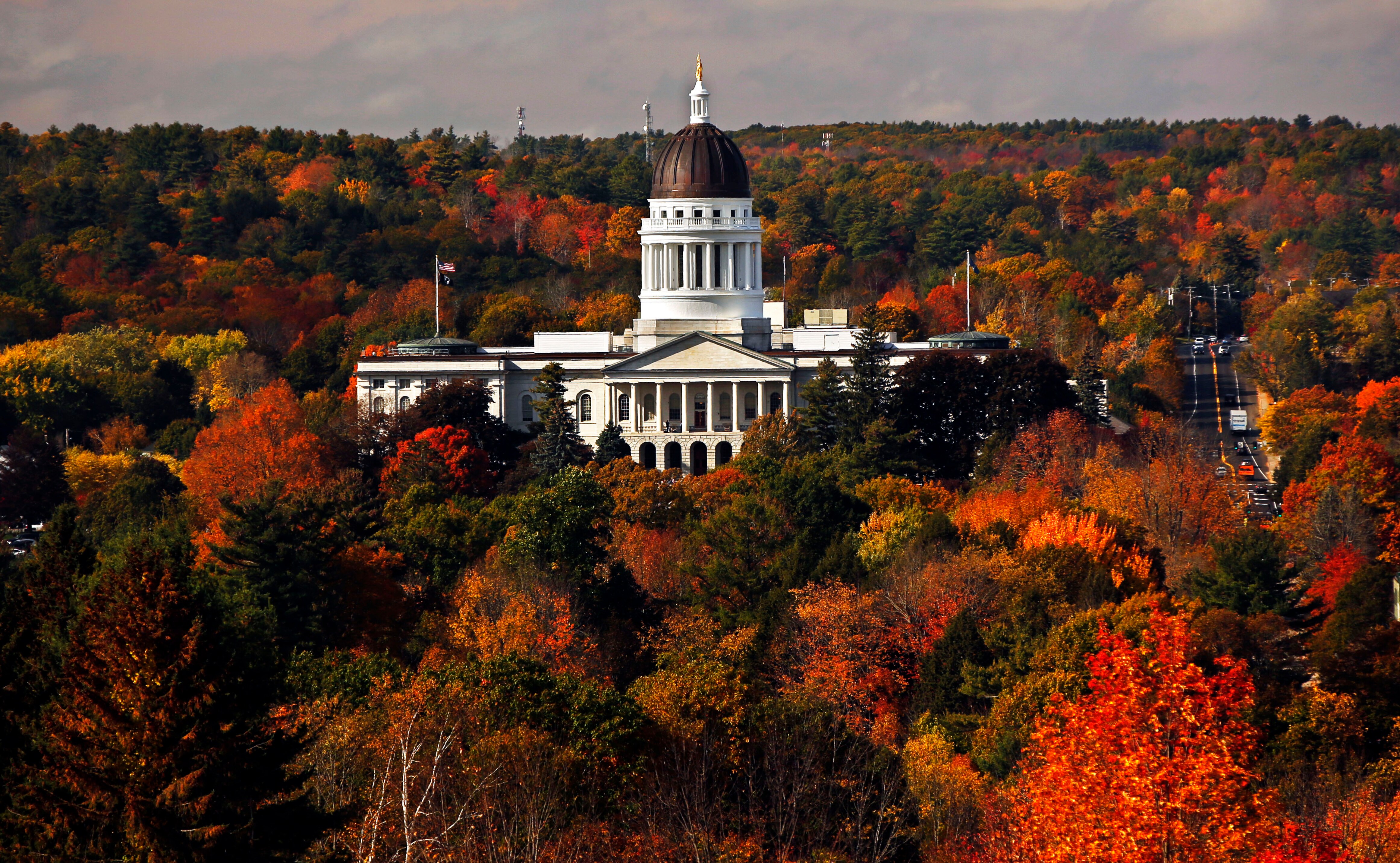 An aerial image of a regal-looking white building. Surrounding it are trees of every shade of yellow, orange, red and green.