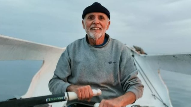 An elderly man smiles while rowing a boat