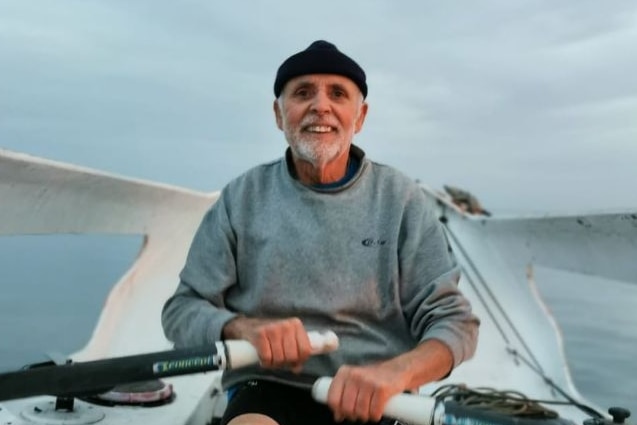 An elderly man smiles while rowing a boat