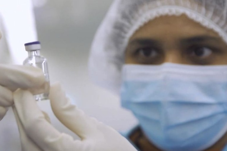 A working wearing protective equipment holding up a vial and looking at it.