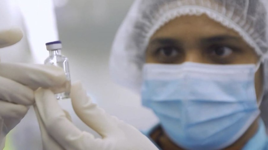 A working wearing protective equipment holding up a vial and looking at it.