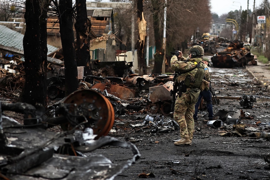 軍の戦闘服を着た兵士が、傷ついた黒ずんだ街路の戦争地帯でビデオテープの損傷