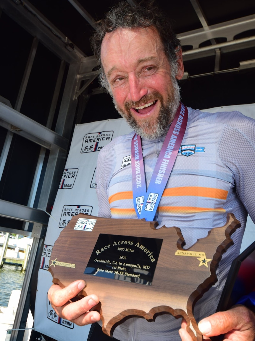 A man wearing a medal holds a plaque in the shape of North America