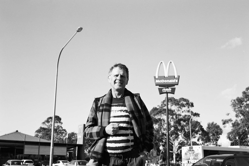 A middle-aged man in casual clothes stands across the road from a McDonalds restaurant in SA.