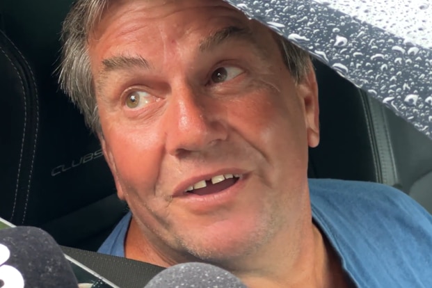 Man in car with microphones in his face.