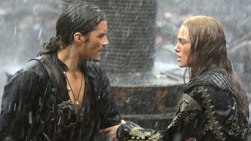 A man and woman stand on a ship in the rain, looking into each other's eyes