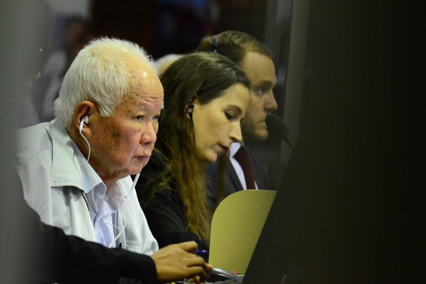 Khieu Samphan, an old man, sits in a courtroom wearing earphones.