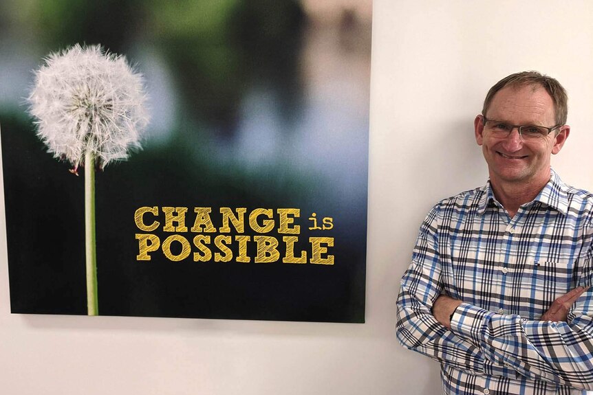 A man smiling at the camera alongside a poster declaring "change is possible"