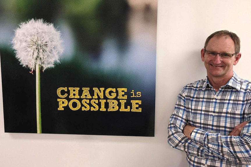 A man smiling at the camera alongside a poster declaring "change is possible"