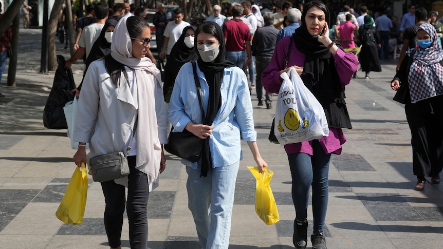 Several hijab-wearing women walking down a busy street carrying shopping bags 