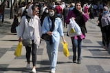 Several hijab-wearing women walking down a busy street carrying shopping bags 