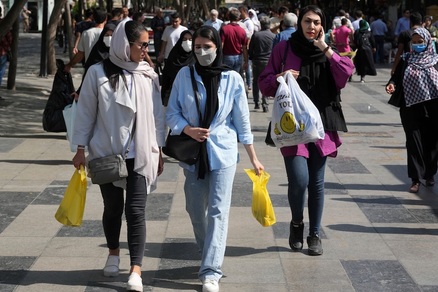 Several hijab-wearing women walking down a busy street carrying shopping bags 