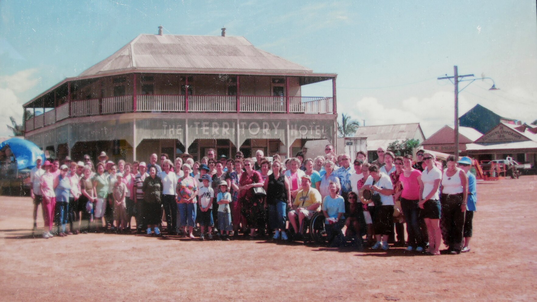 A group of people stand outside an old-fashioned two-storey pub with a sign reading 'The Territory Hotel'