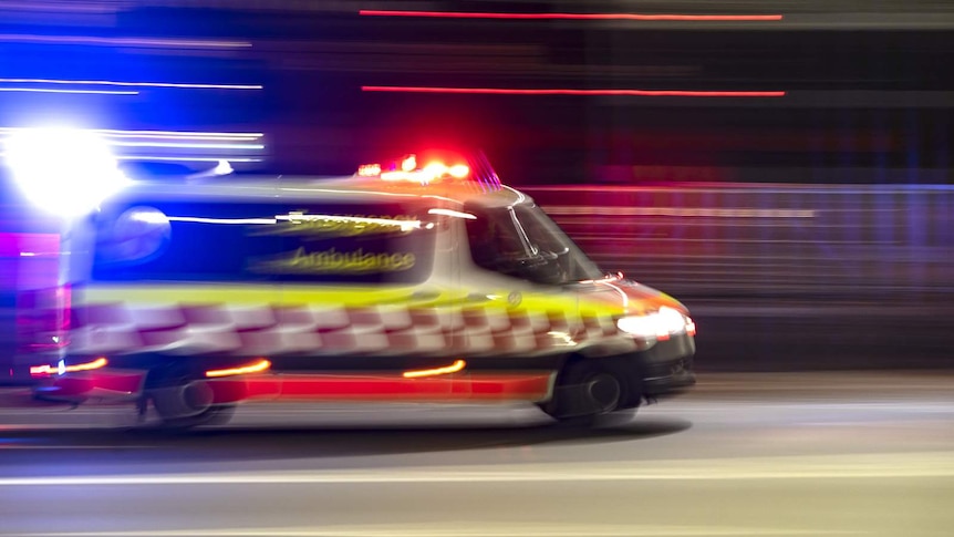An ambulance, captured in motion blur, crosses Sydney Harbour Bridge at night, with its top lights on. Street lights flare.