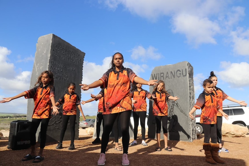 Wide shot of a group of dancers performing in front of a monument.