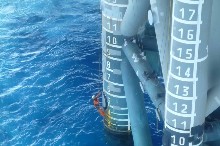 Peter McGregor hanging from ropes and painting the pylons of an oil rig.