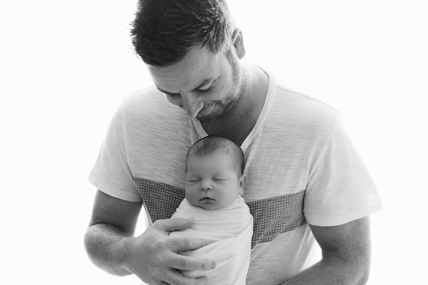 A black and white portrait of a man holding a newborn baby.