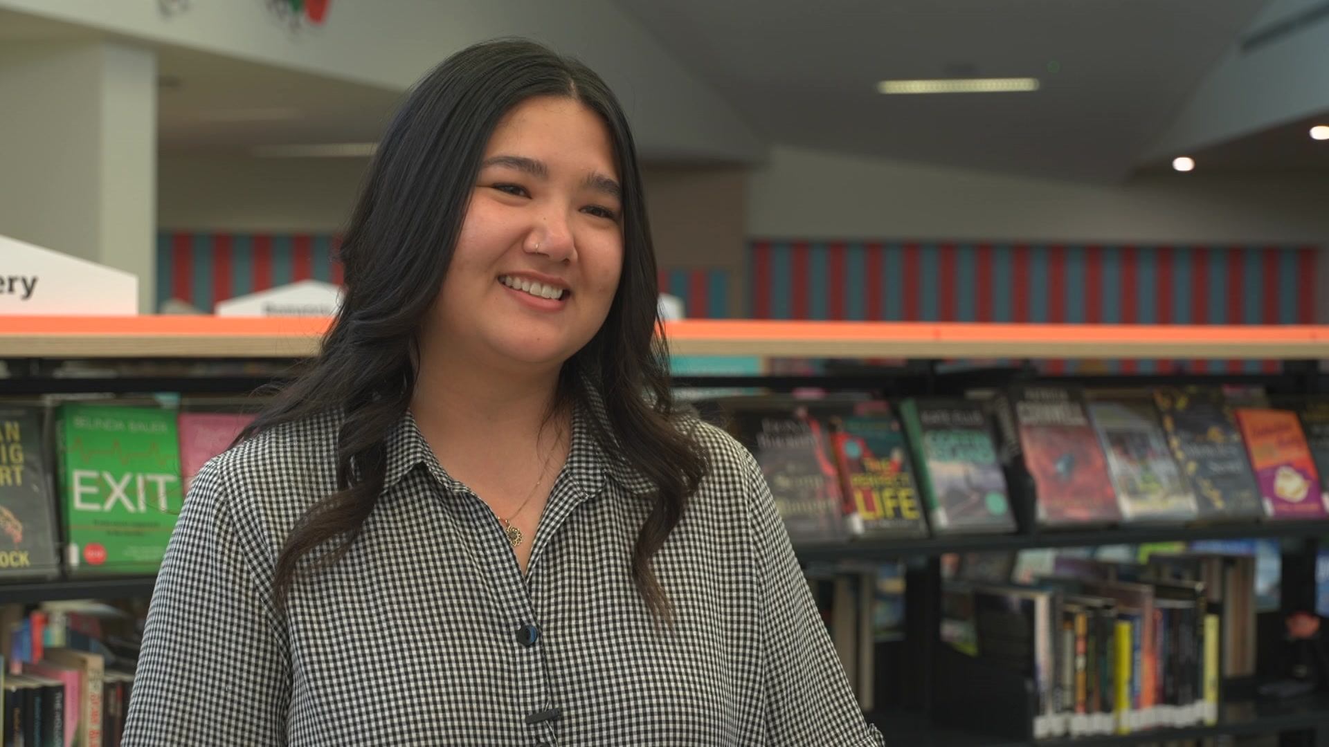 A woman smiles standing next to book shelves