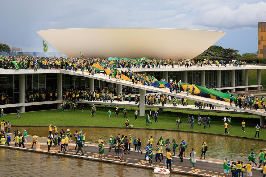 Crowds of people draped in the Brazilian flag walk across teh grounds and over a building. 