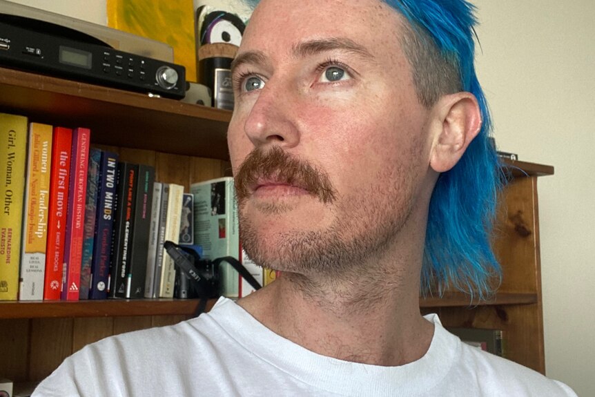 Selfie of a man with blue hair shaved on sides and long at back. 