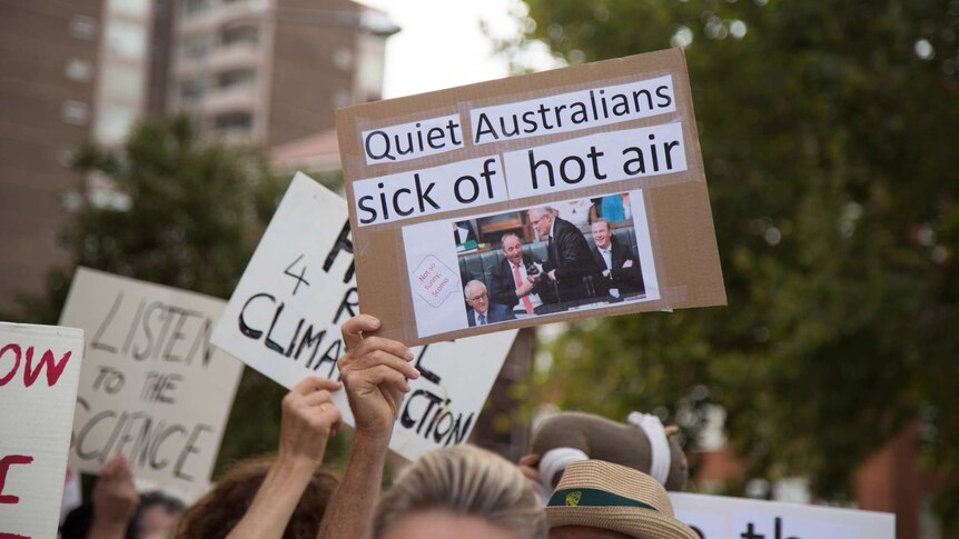 A hand holds up a placard at a demonstration reading: Quiet Australians sick of hot air
