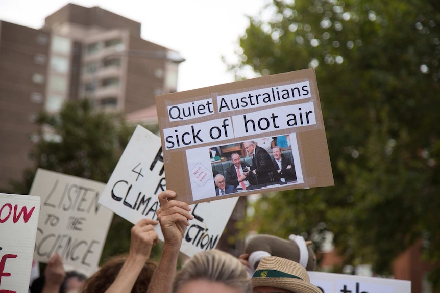 A hand holds up a placard at a demonstration reading: Quiet Australians sick of hot air