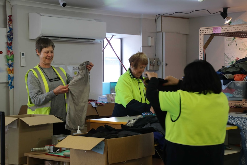 Three volunteers sort clothes in a charity shop.