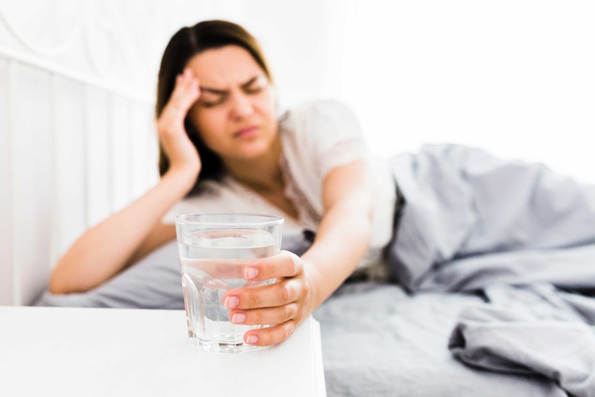 Woman in bed reaching for glass of water