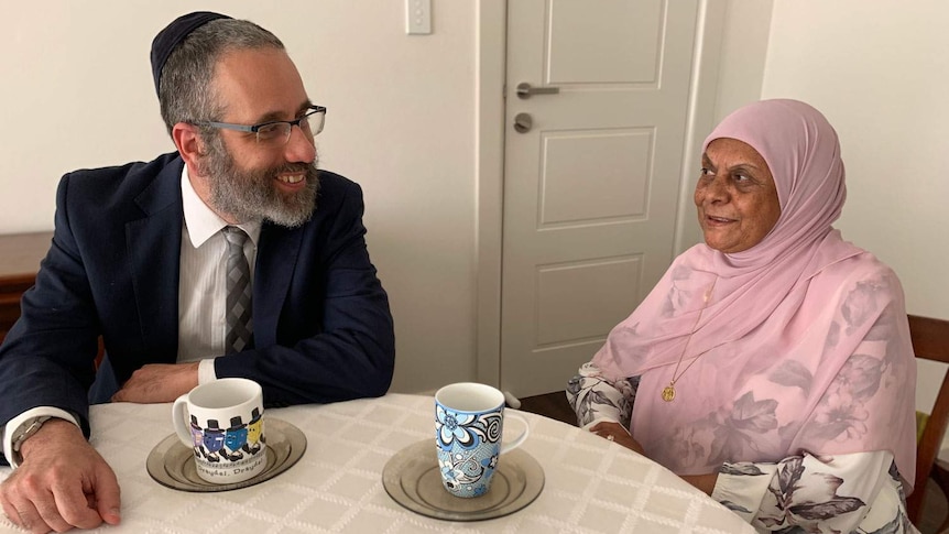 Rabbi Zalman Kastel sits at a table chatting with Madenia Abdurahman.