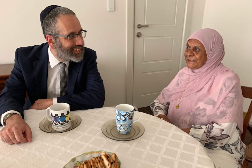 Rabbi Zalman Kastel sits at a table chatting with Madenia Abdurahman.