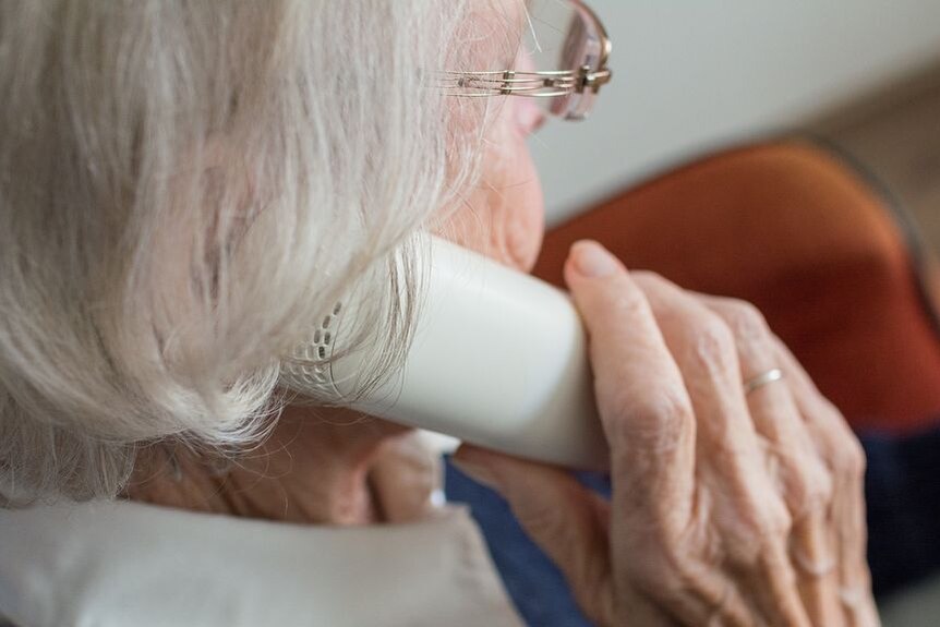 An elderly woman holds a phone up to her ear.