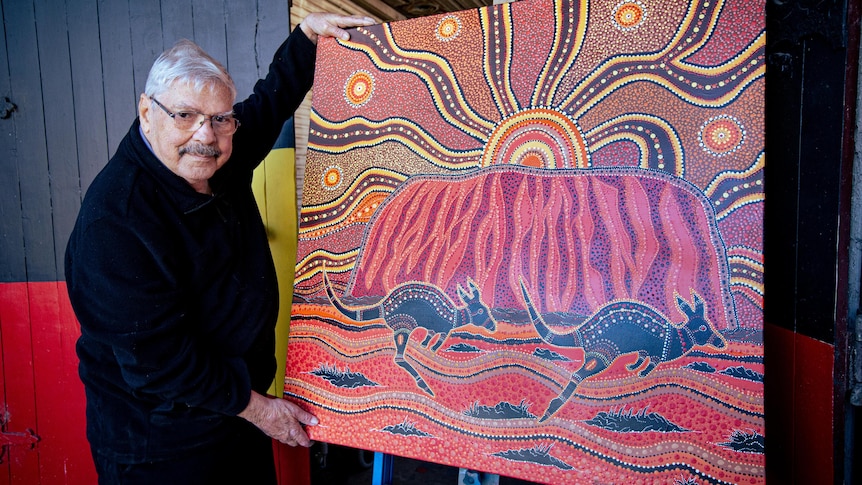 an indigenous man standing next to a large canvas
