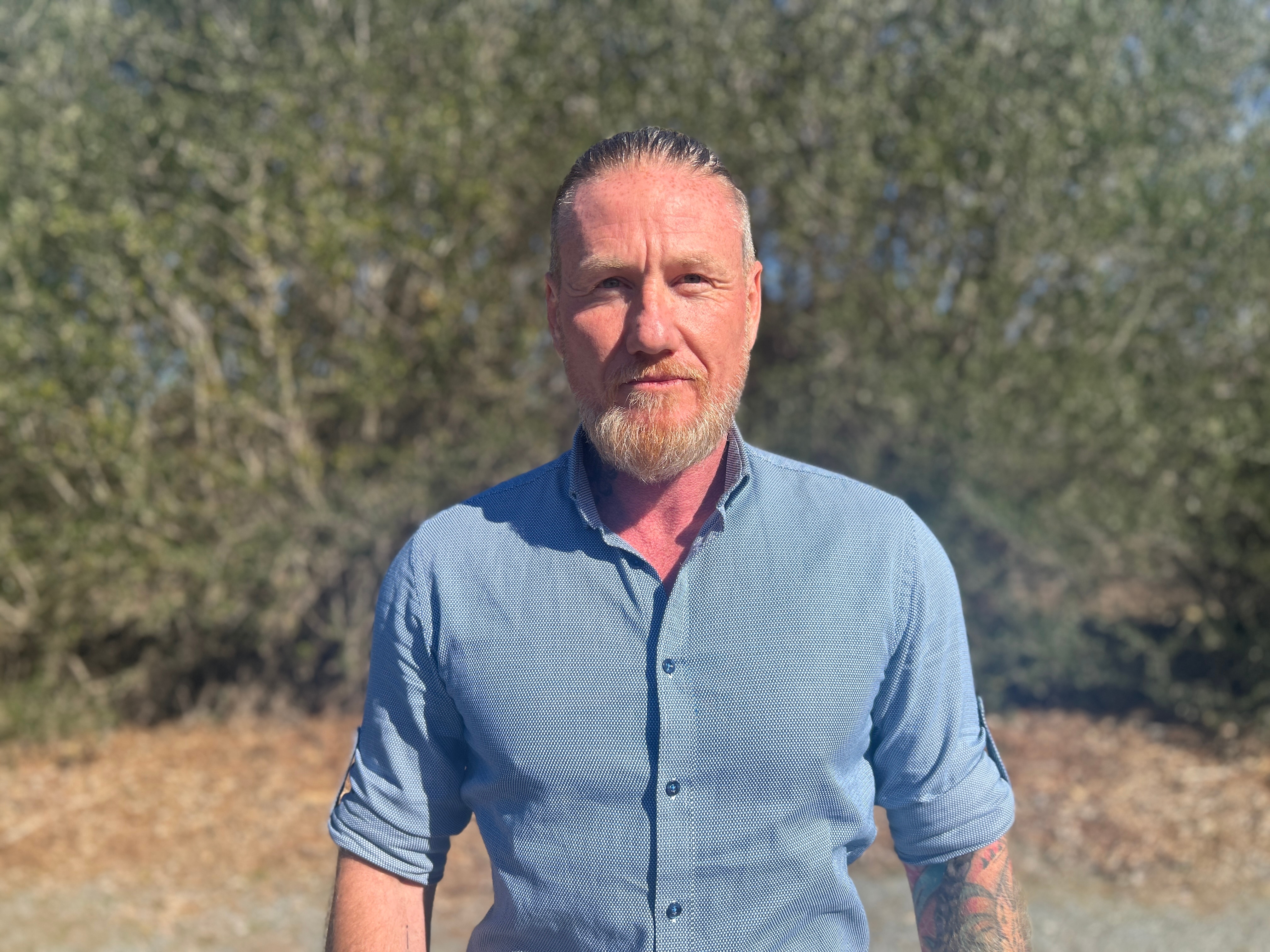 Un hombre de pelo gris y barba que vestía una camisa azul con botones.