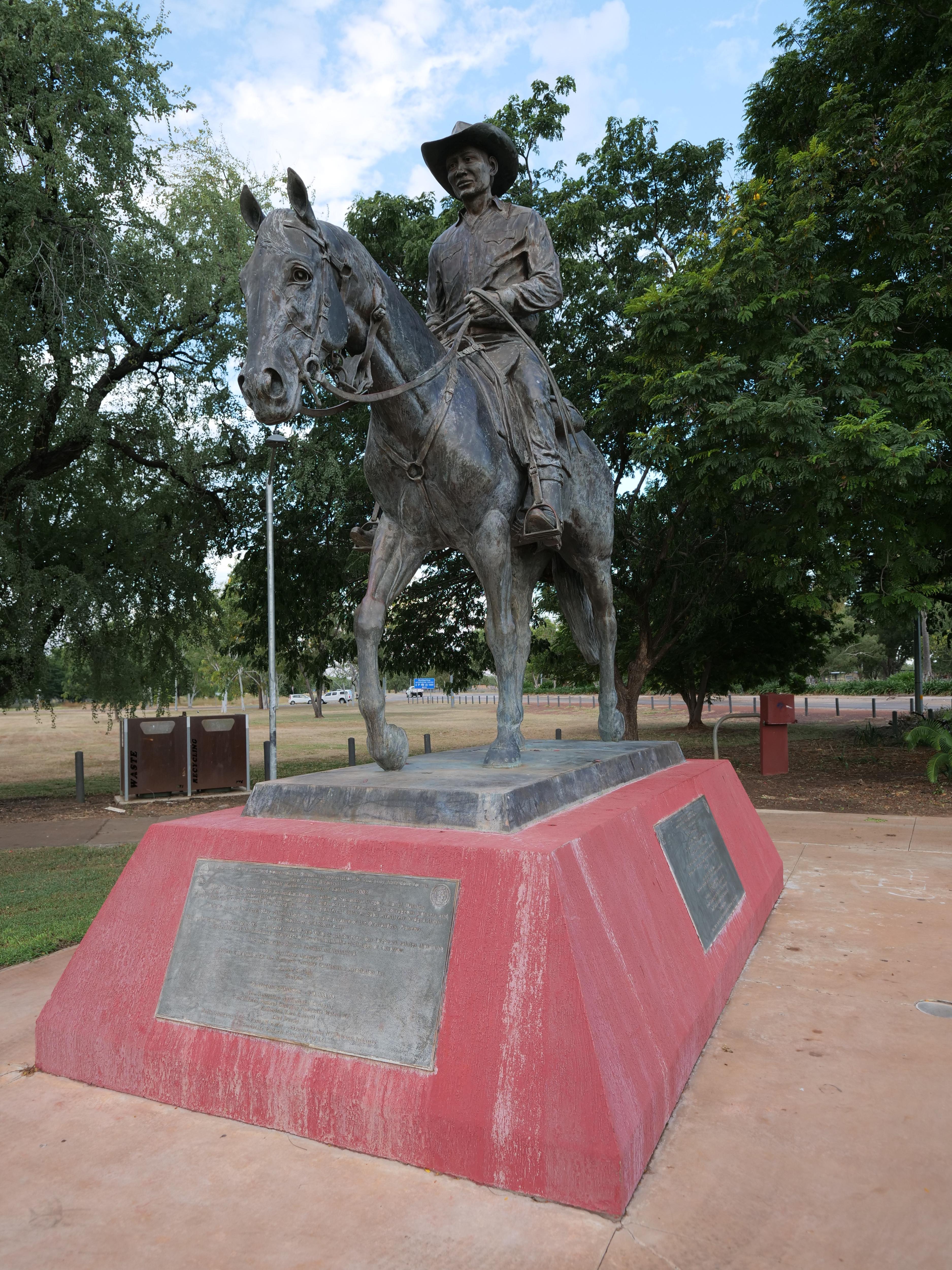 A bronze statue of a man on a horse on a red concrete base